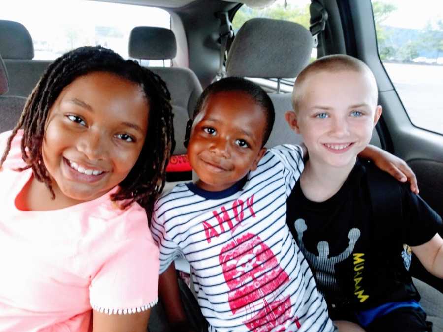 Three siblings sit in the back of their parents' van