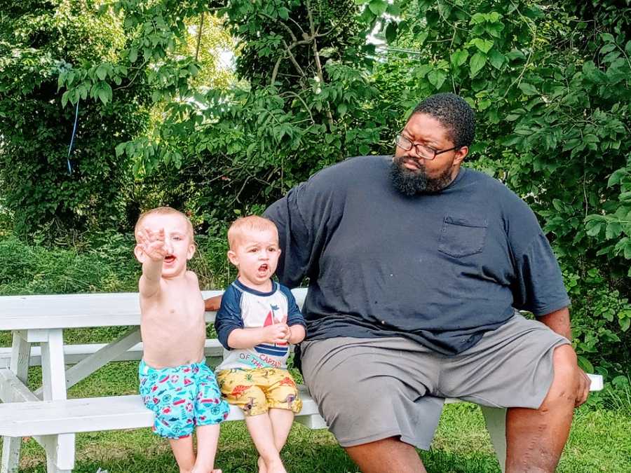 A father sits on a bench with his twin sons