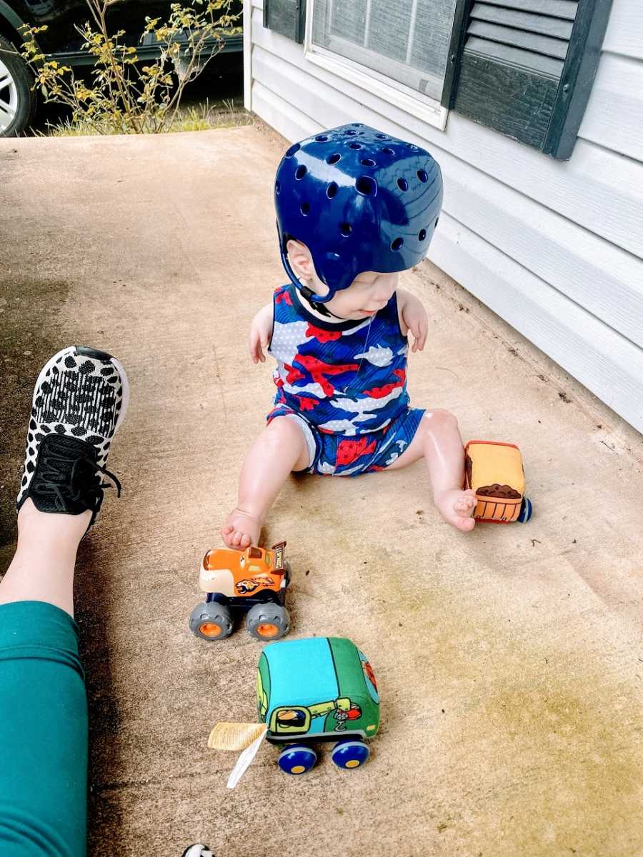 A little boy with no arms wearing a helmet and playing with trucks