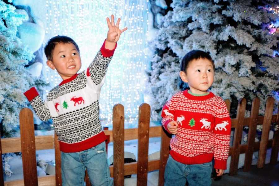 A pair of boys stand together wearing Christmas sweaters