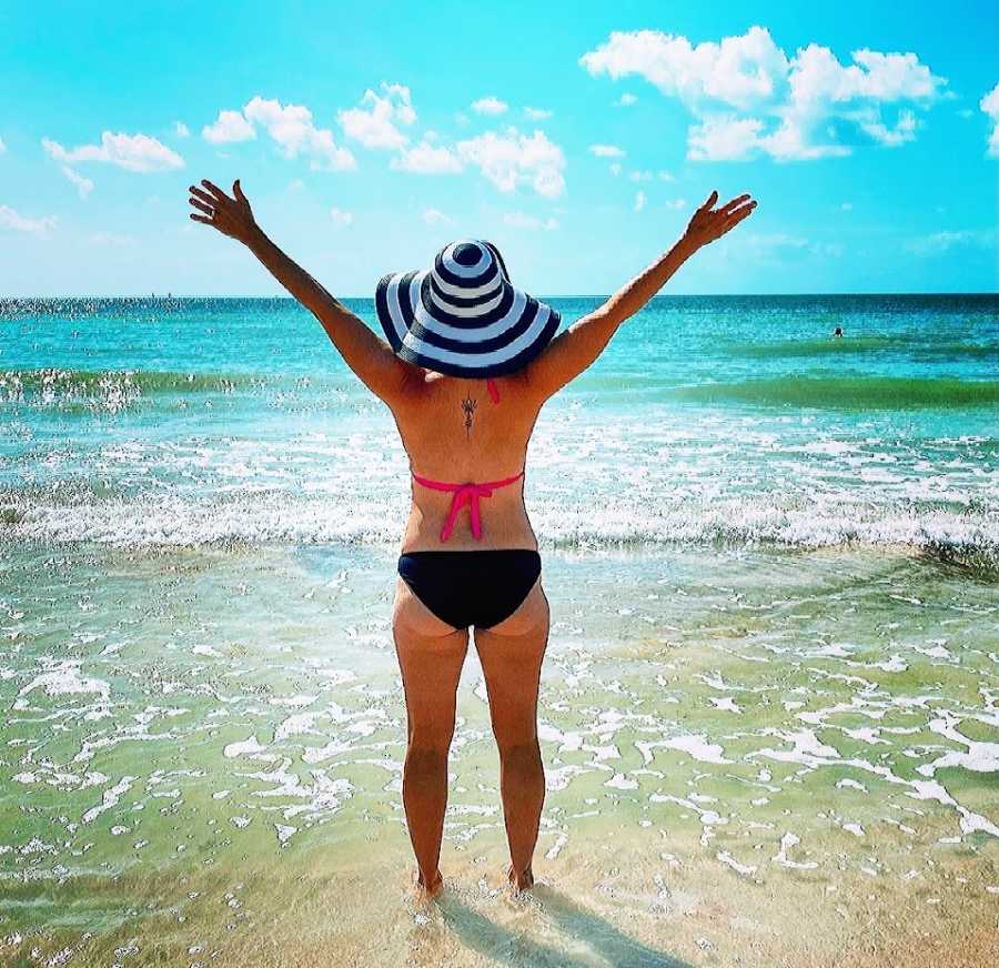 A woman stands by the beach with her arms outstretched