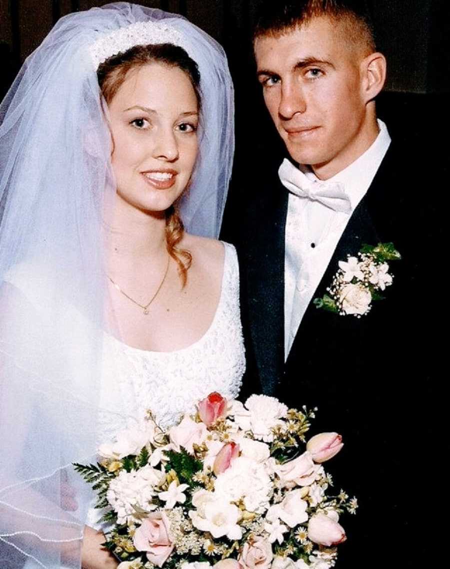 A bride holds flowers and stands with her groom