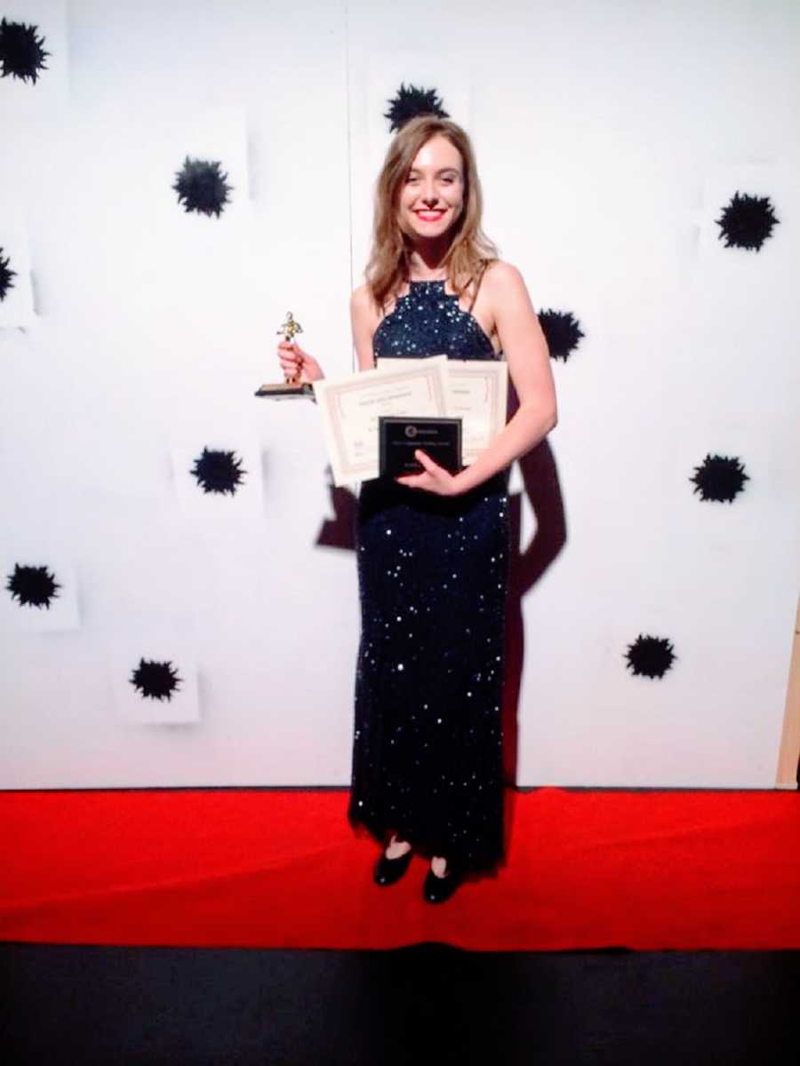 A woman wearing a black dress holds up an award