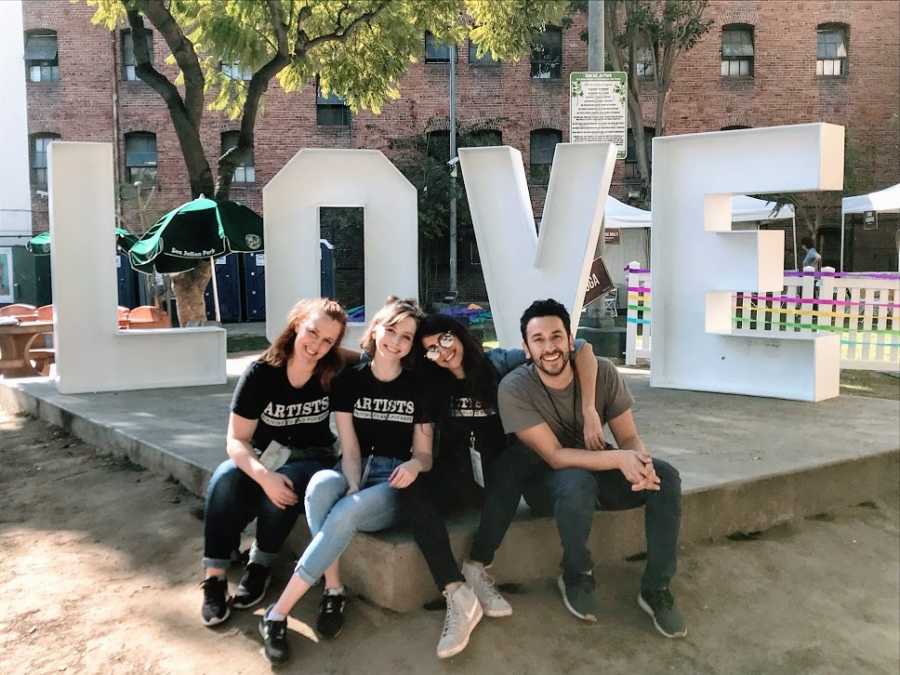 A young woman sits with her friends in front of a LOVE sign