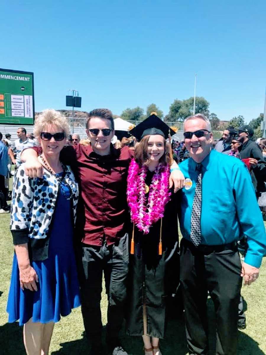 A young woman wearing a cap and gown stands with her family