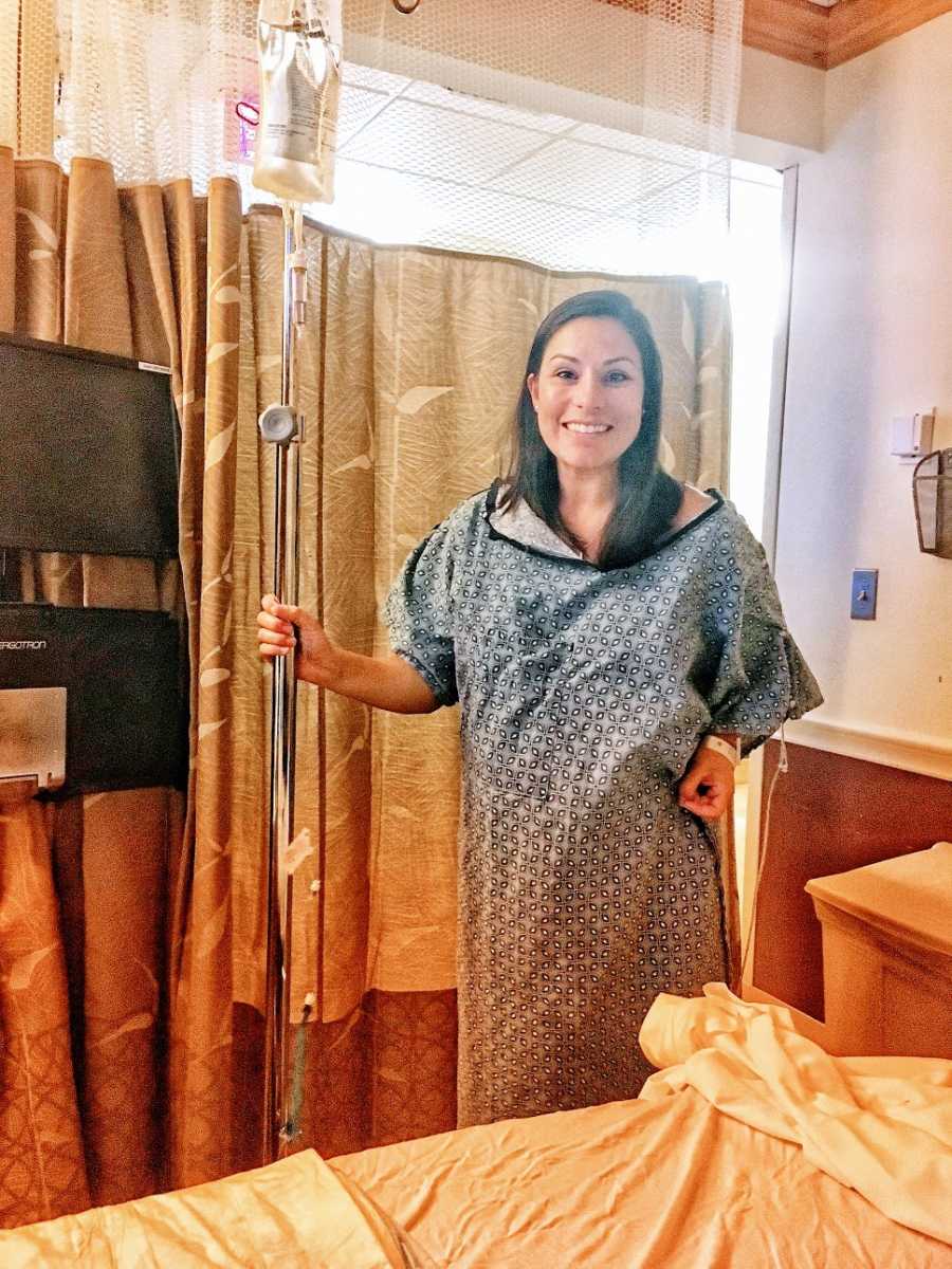 A woman stands wearing a hospital gown