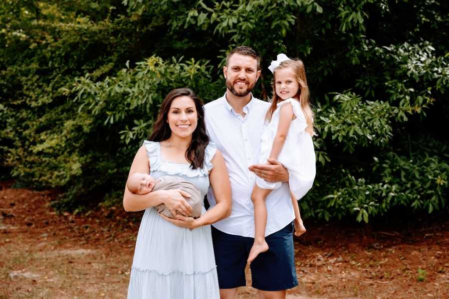 Parents hold their two children outdoors by trees