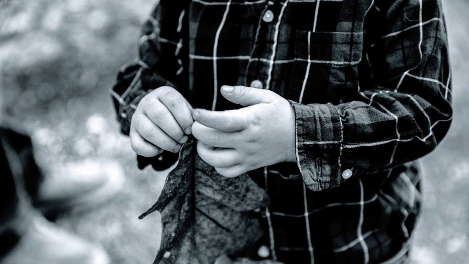 A boy wearing a plaid shirt picks at his fingernails