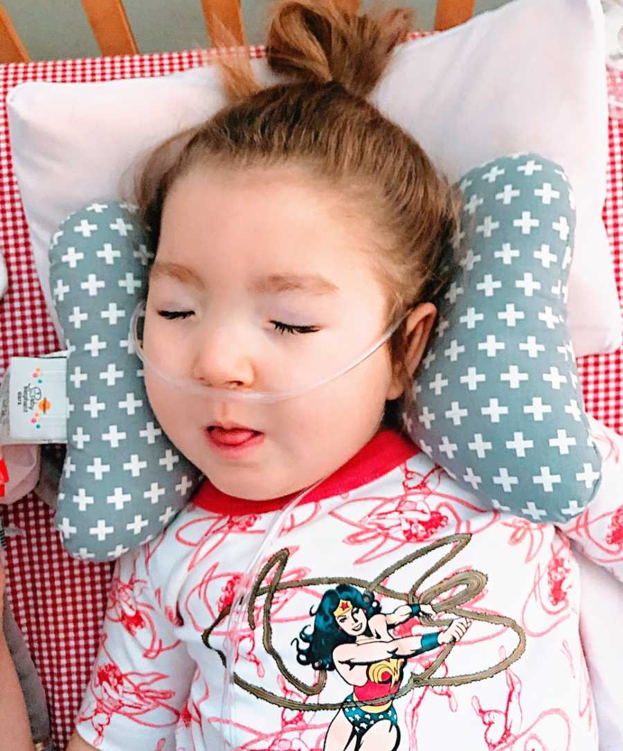 A little girl with epilepsy lies on a pillow wearing an oxygen tube