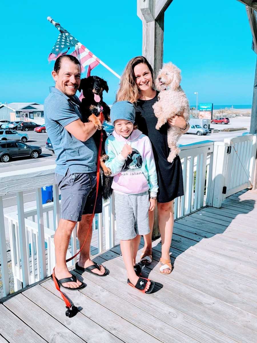 A couple stand with their dogs and their son on their front porch