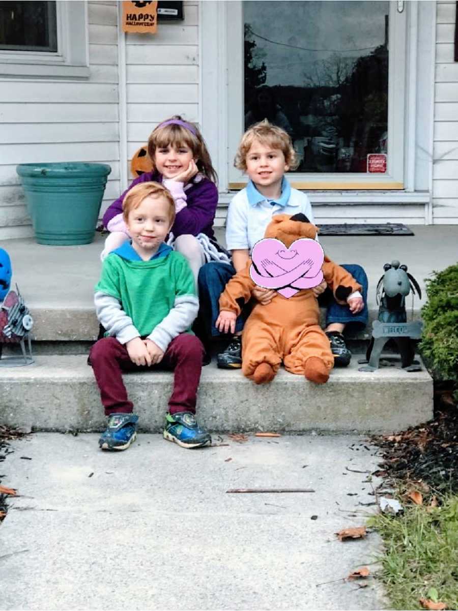 Three children sit on steps with their foster brother