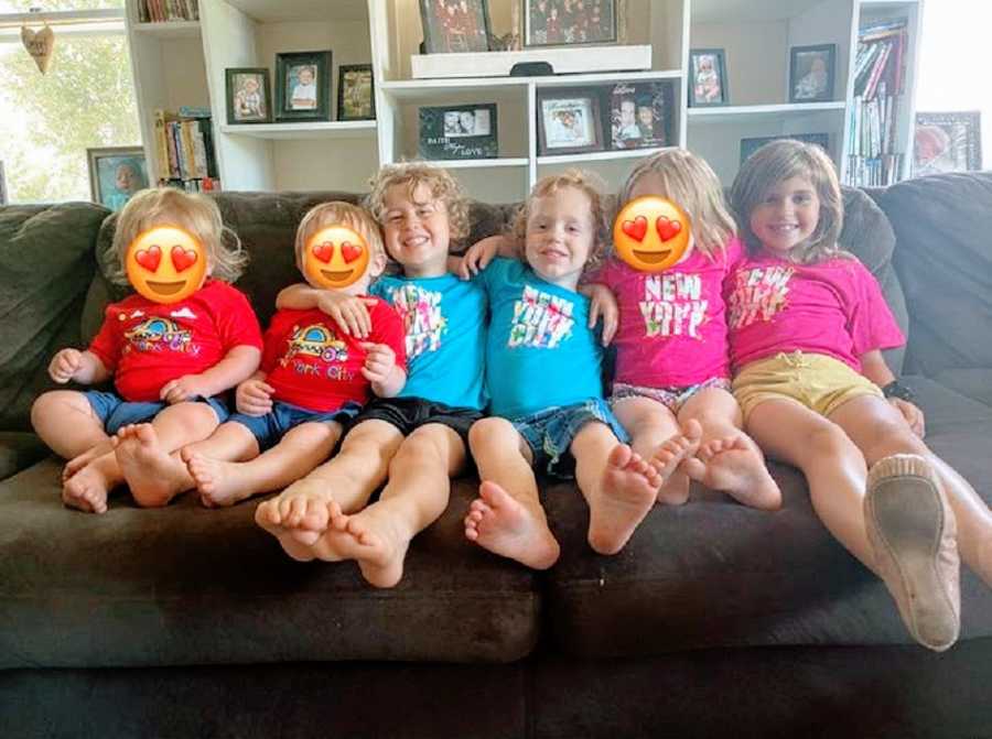 Six children sit together on a couch in matching T-shirts