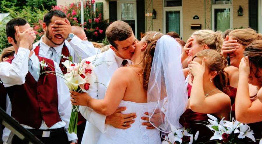 A groom kisses a bride while onlookers cover their eyes