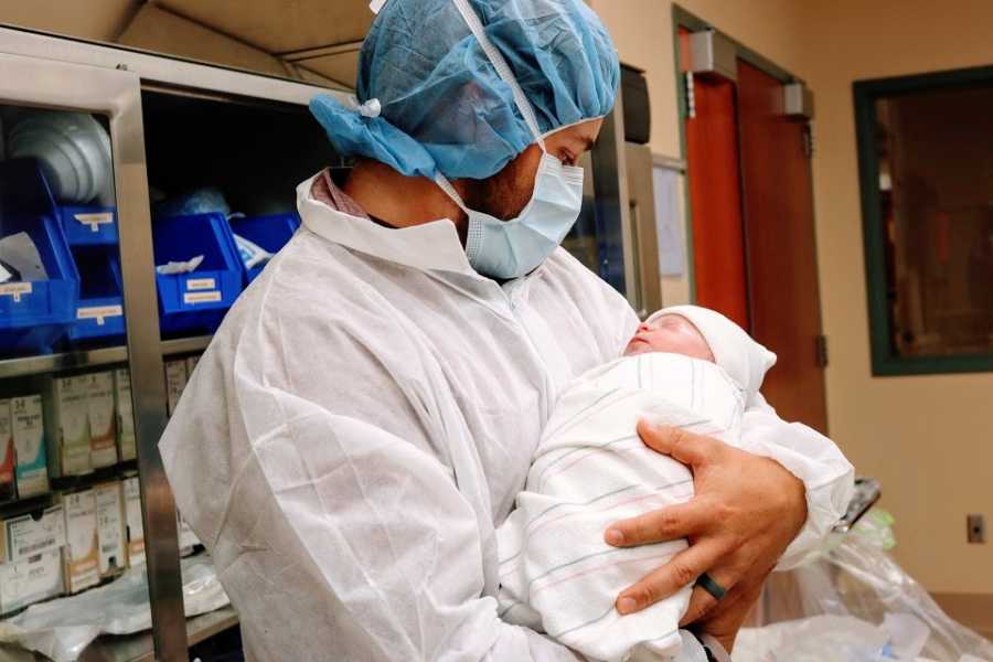 A man in a surgical mask holds a swaddled baby boy