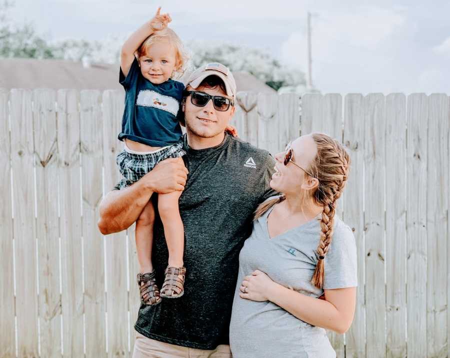 A couple and their son stand outside in front of a fence