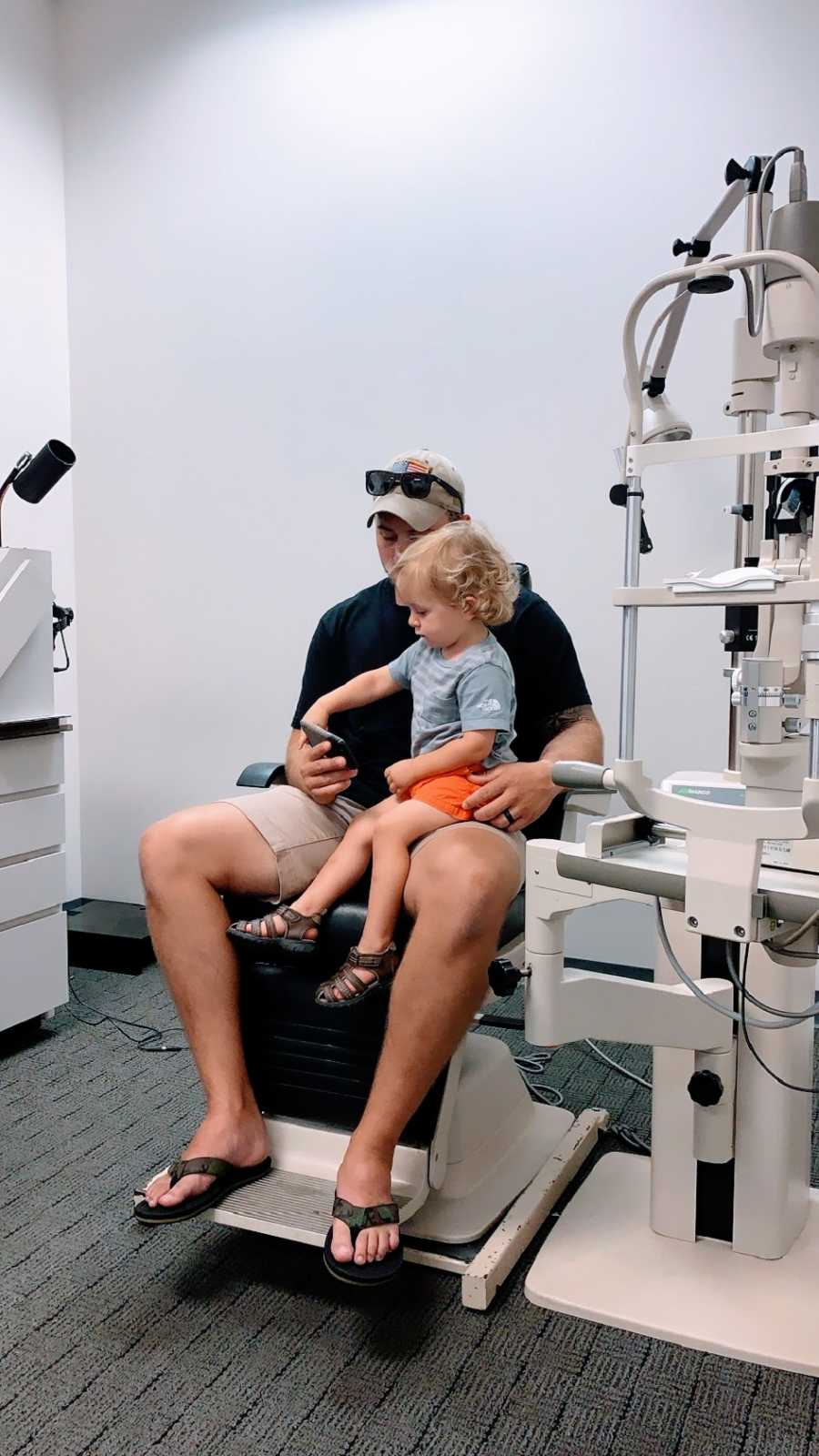 A little boy sits on his father's lap at a doctor's appointment