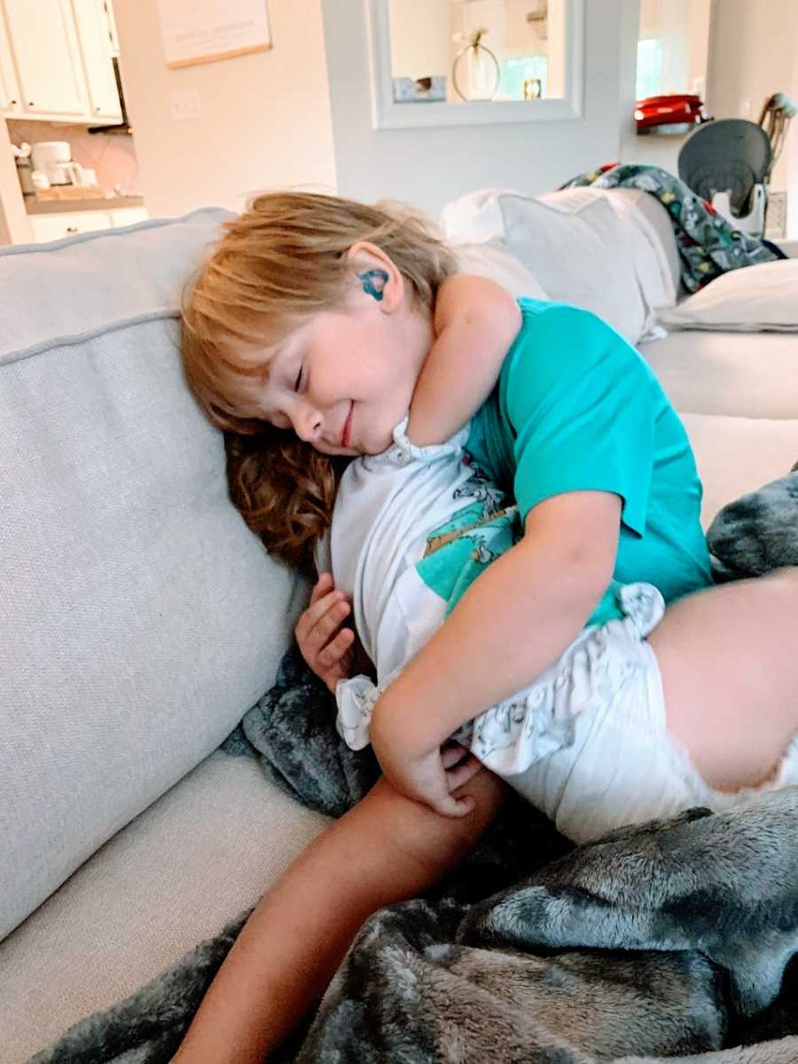 A little boy with hearing aids hugs his little sister