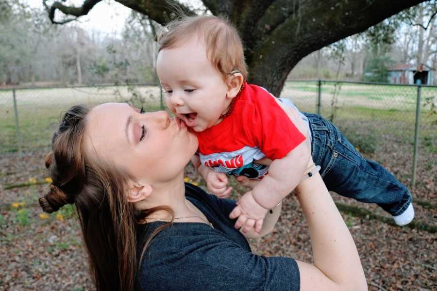 A mother holds her baby boy over her head and kisses him