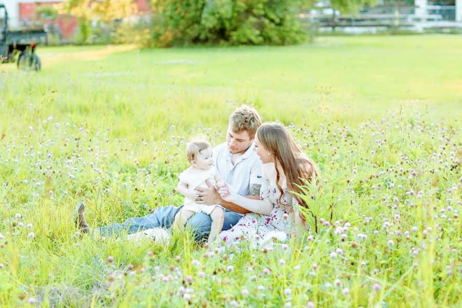 Parents sit in a field with their young son