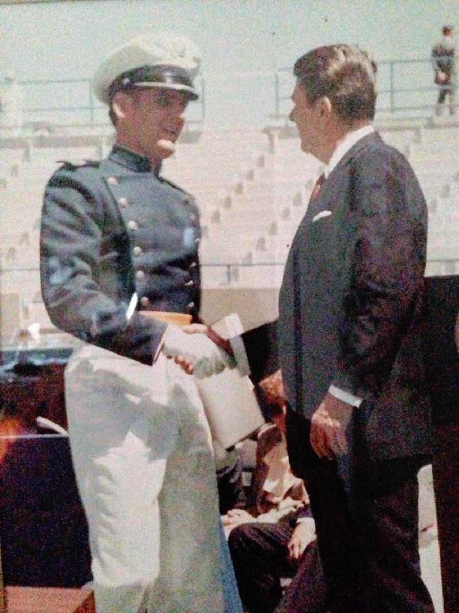 A young man in a military uniform shakes another man's hand