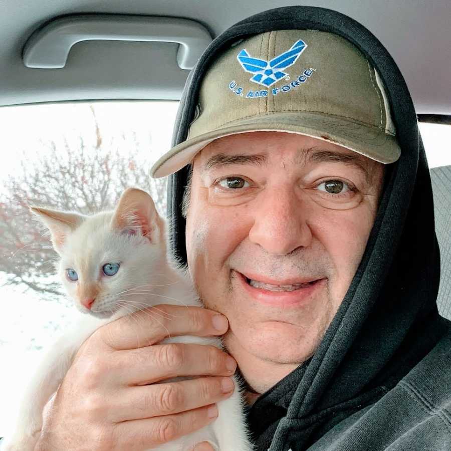 A man sits in a car holding up a white kitten