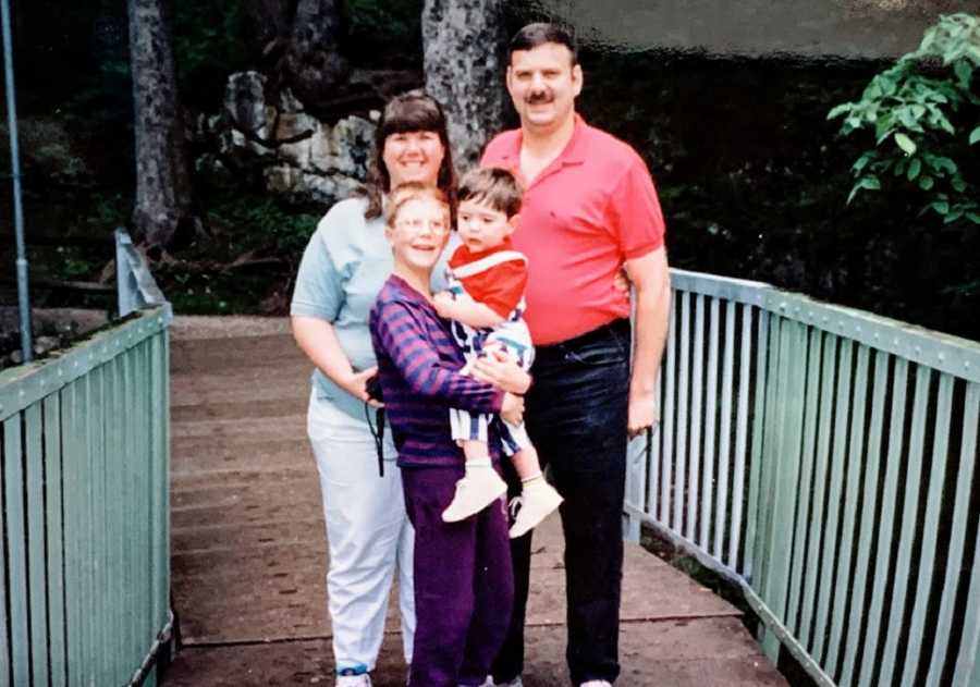 A family of four stand together on a bridge