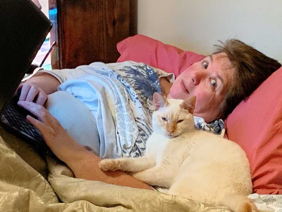 A woman lies in bed with a white cat