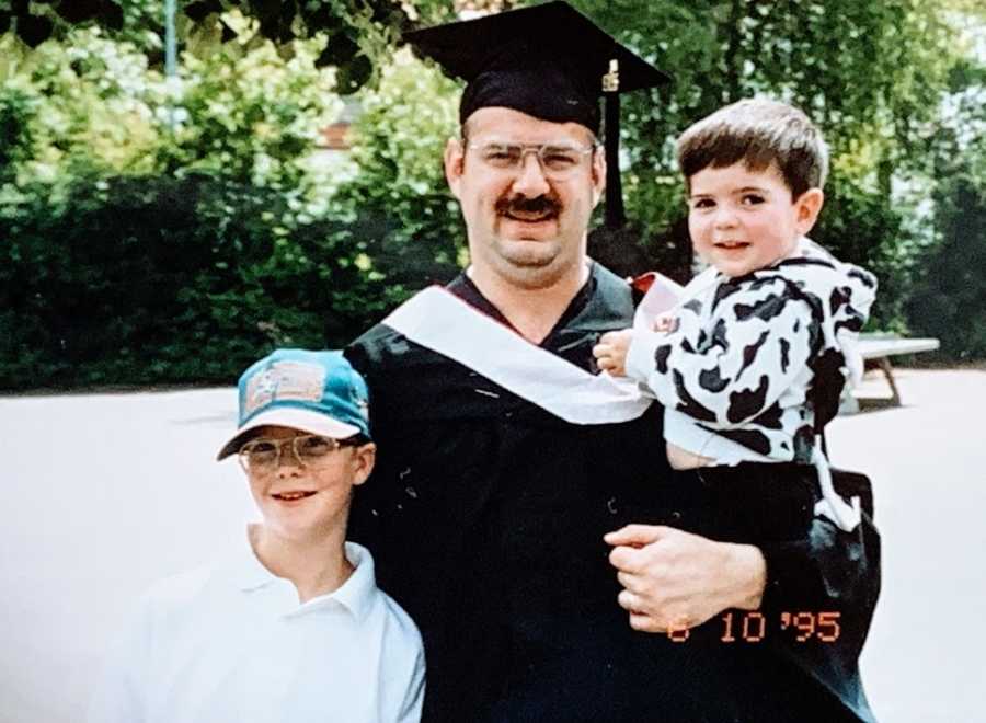 A man in a cap and gown stands with his two young sons