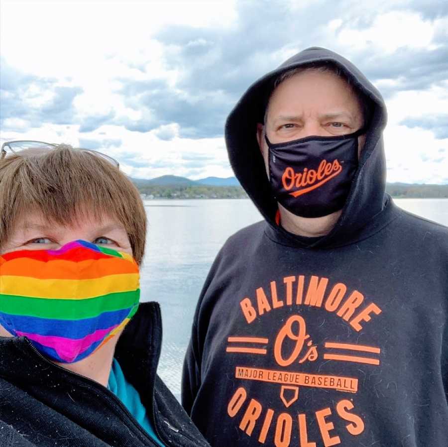 A couple stand together wearing masks