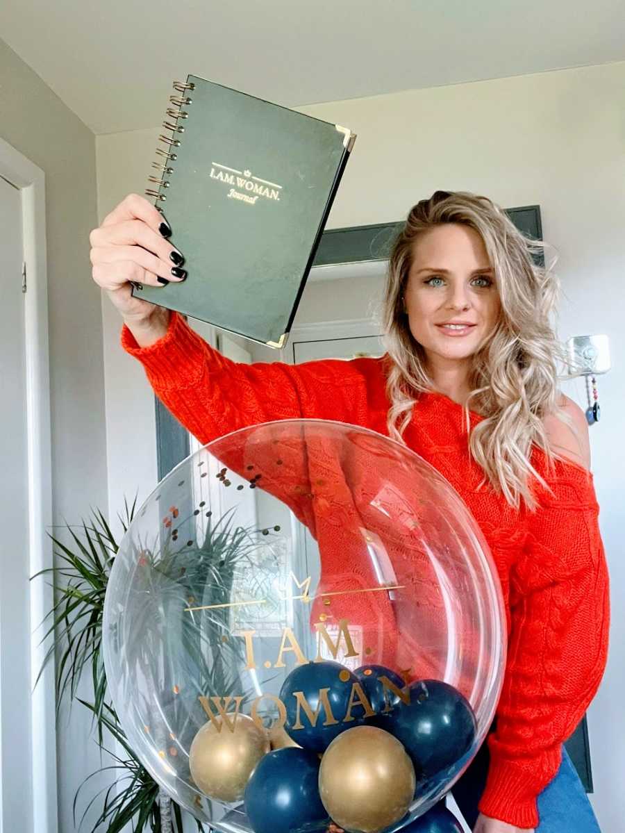 A woman in a red shirt holds up a black journal