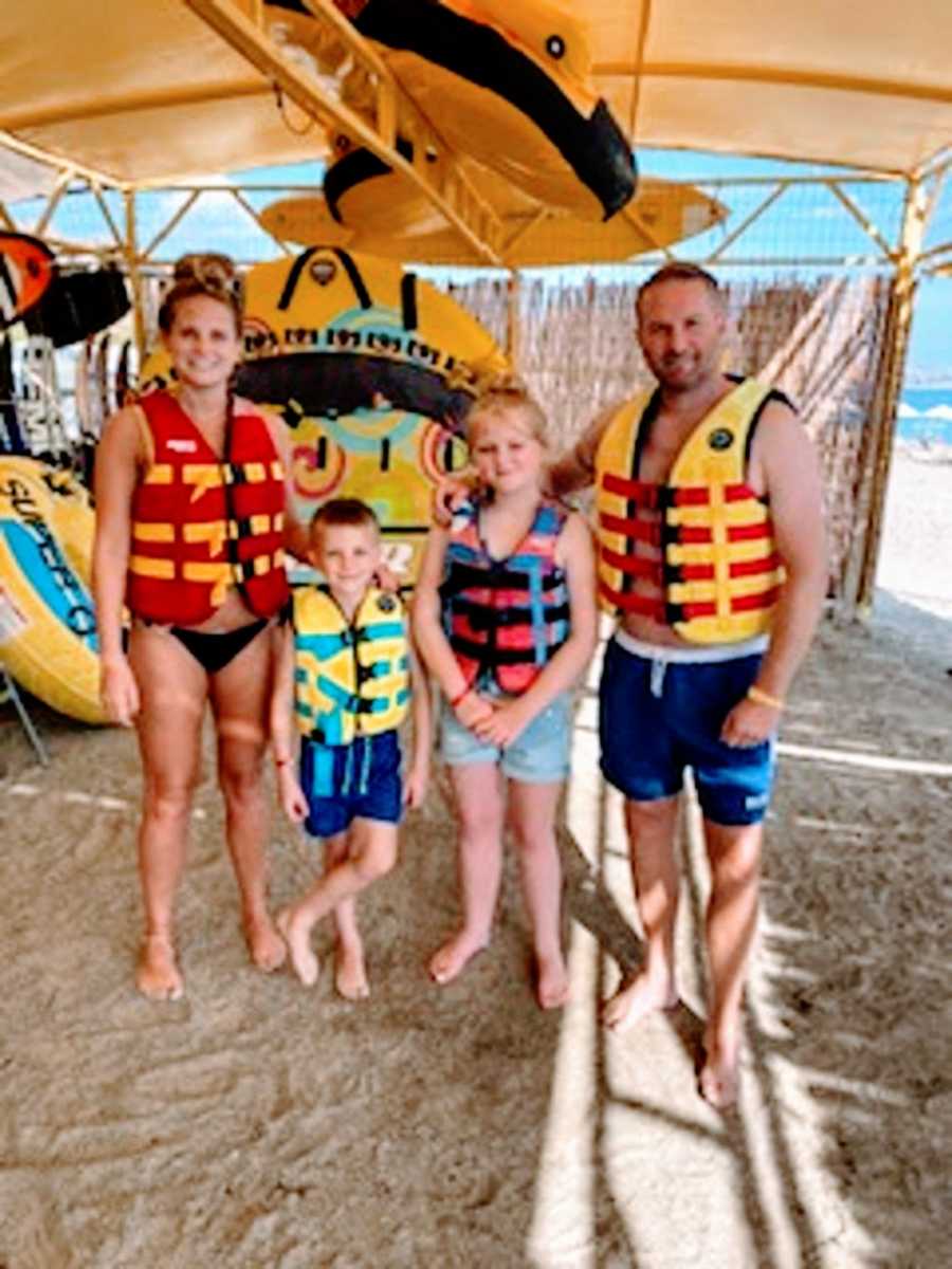 Parents and their two kids wear life vests on a beach