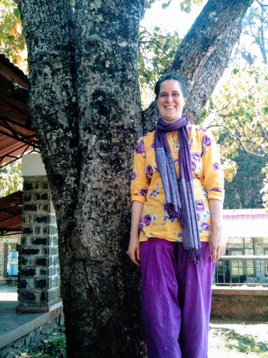 A woman wearing purple and yellow stands by a tree