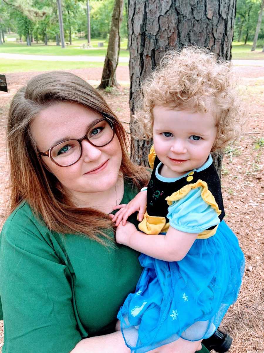 A mother holds her young daughter who is wearing a dress