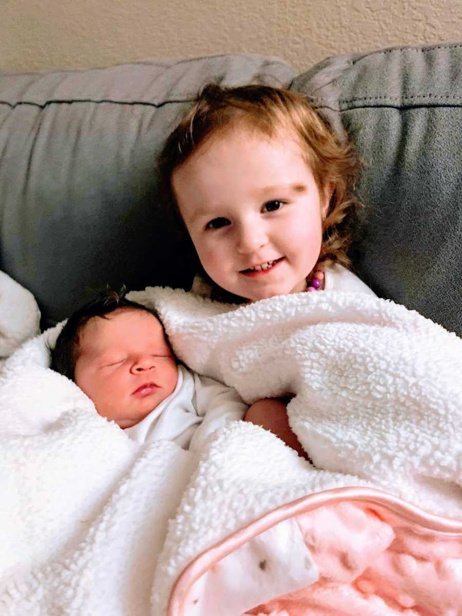 A little girl and her baby sister sit wrapped in blankets