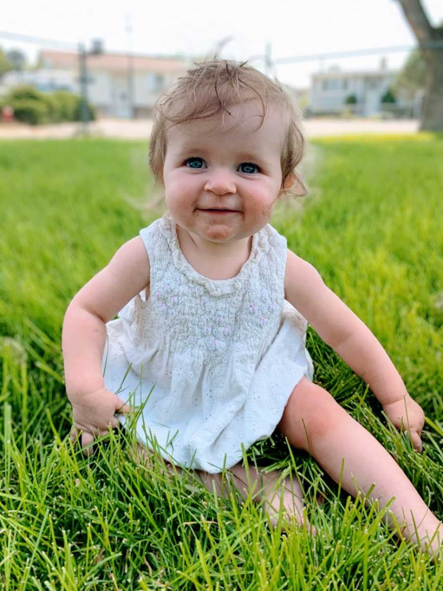 A baby girl sits alone in the grass