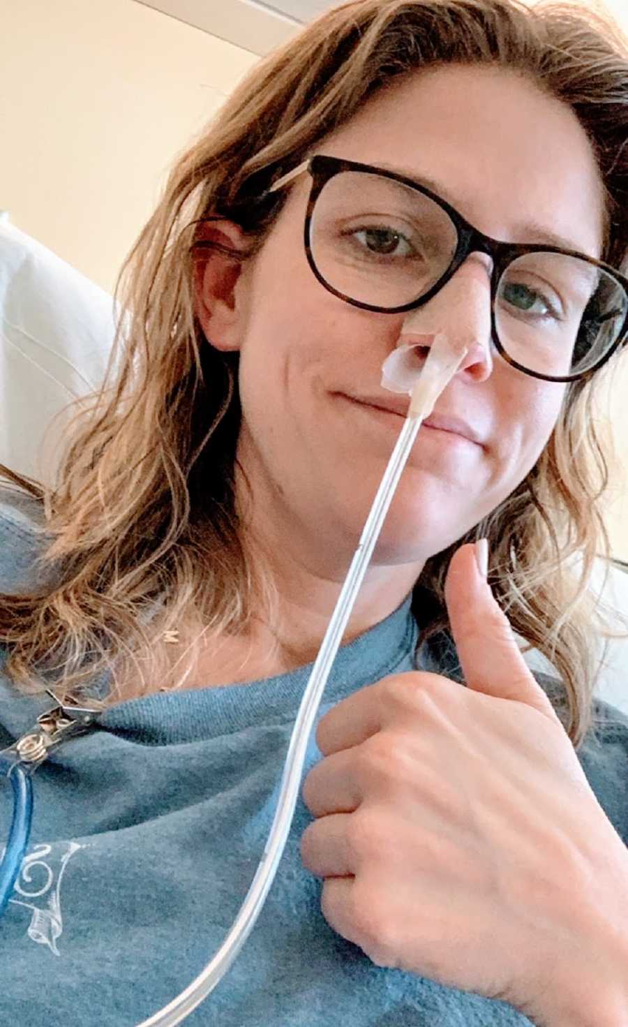 A woman with a tube in her nose gives a thumbs up