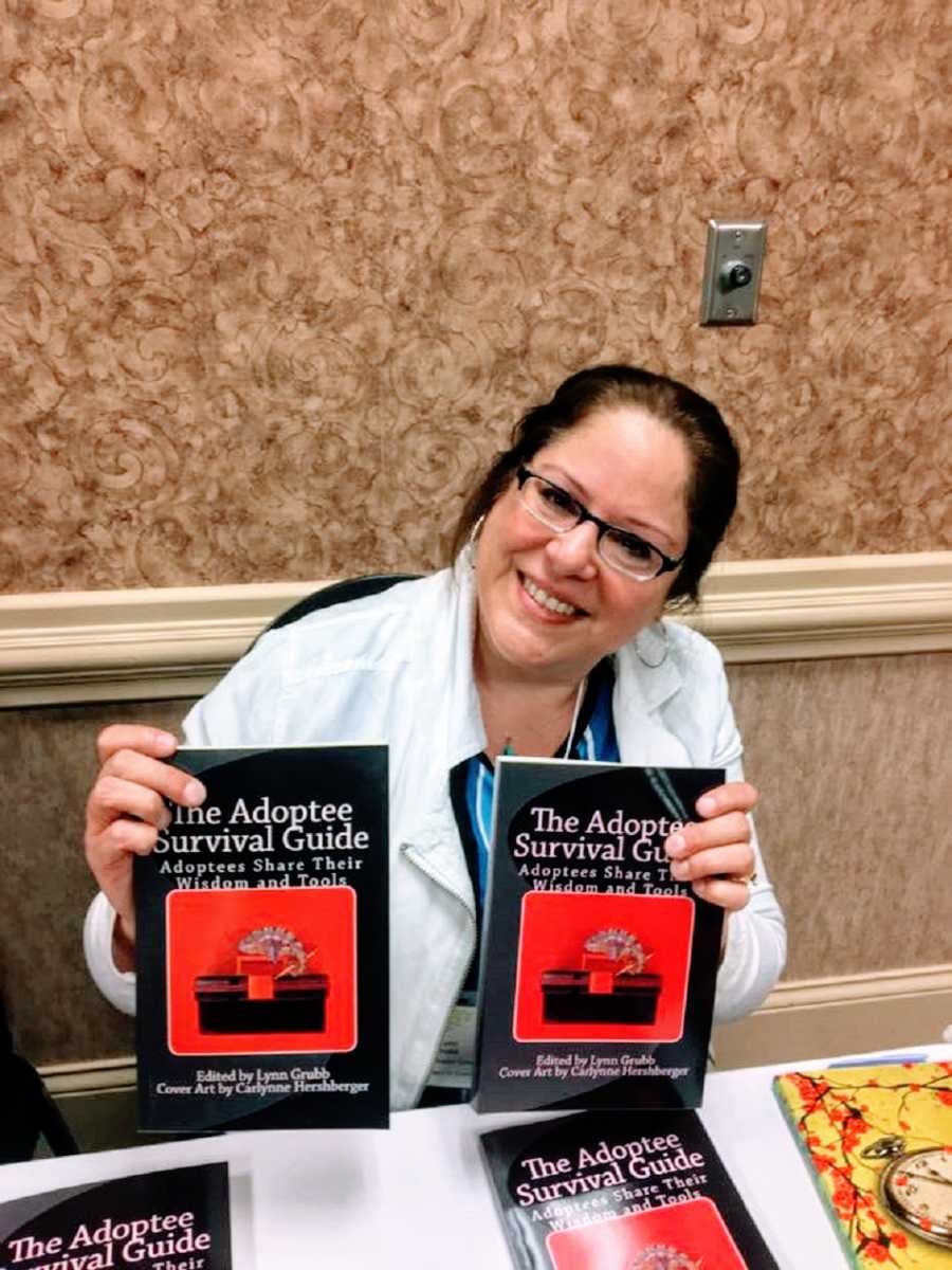 A woman sits at a table holding up two books