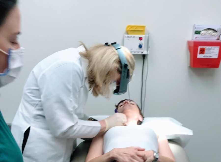 A woman lies on a table while a doctor operates on her neck