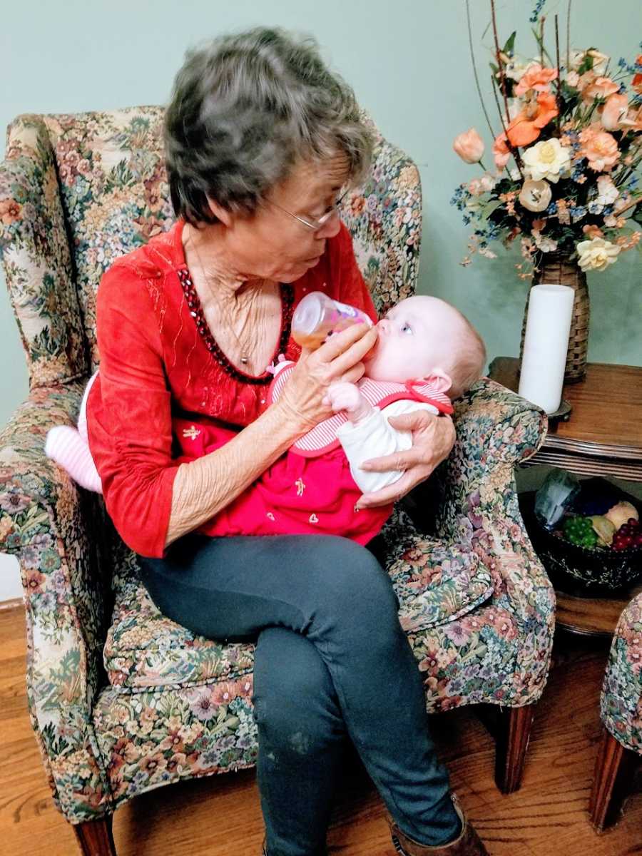 An older woman bottle feeds a baby girl