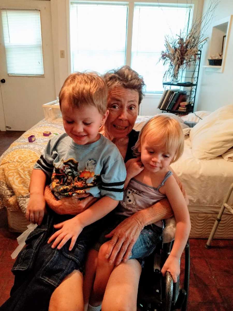 An older woman sits in a wheelchair with her two grandchildren