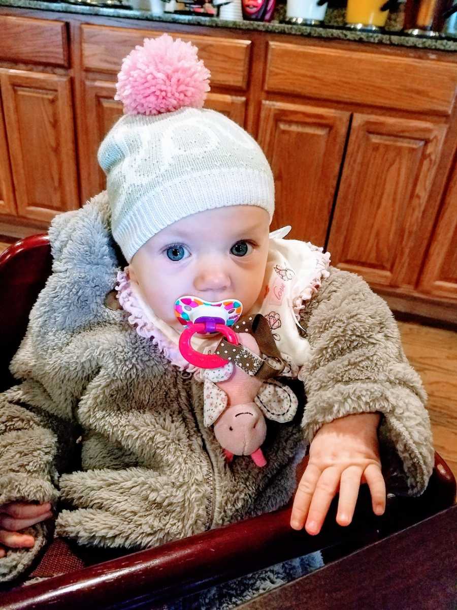 A baby girl with a pacifier wearing a winter coat and hat