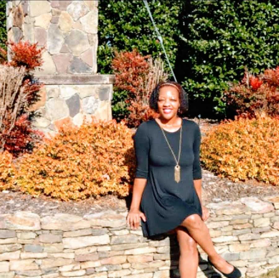 A woman sits on a stone wall in a black dress