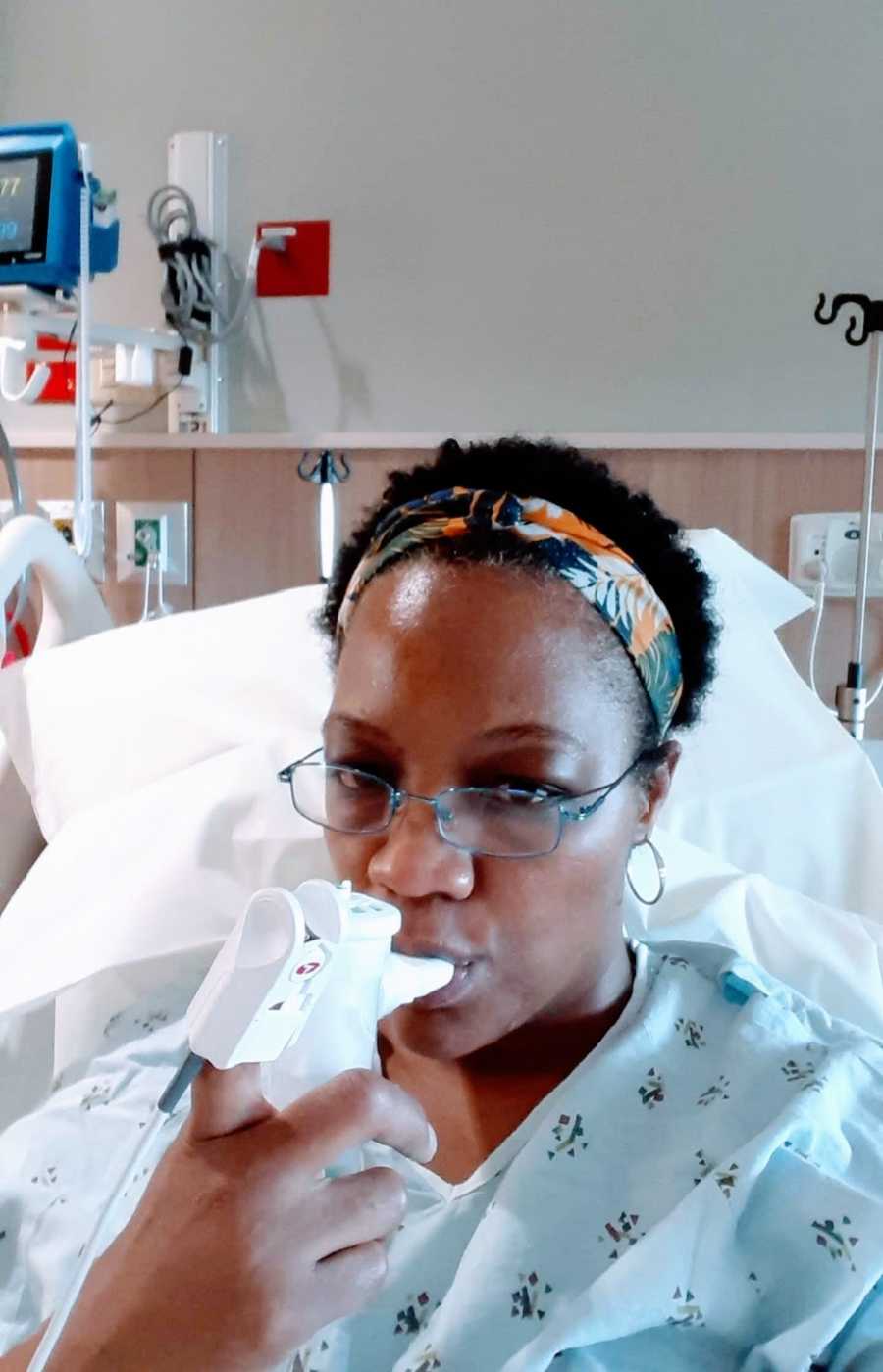 A woman sitting in a hospital room uses an inhaler