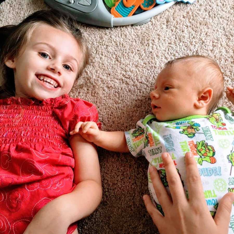 A little girl lies on the floor with her baby brother