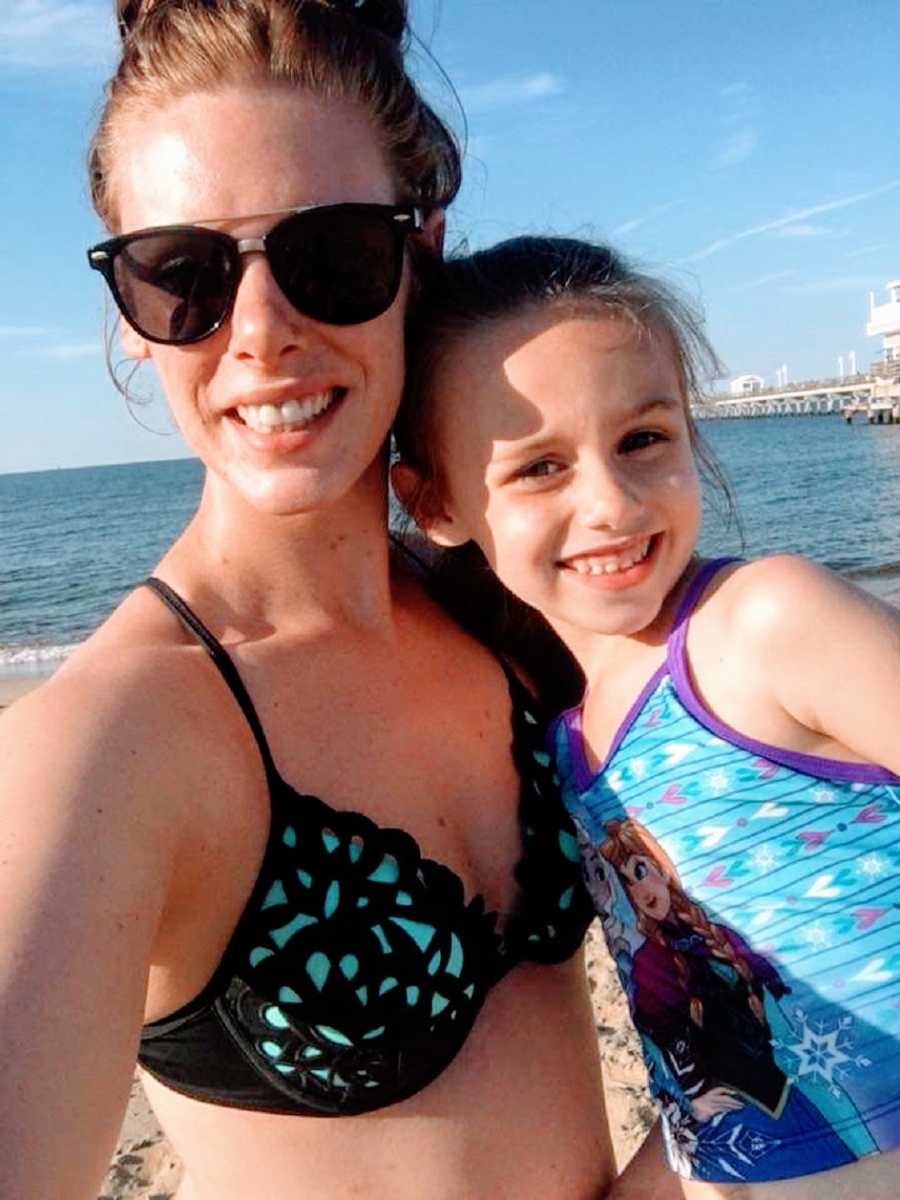 A girl and her mother wearing swimsuits at the beach