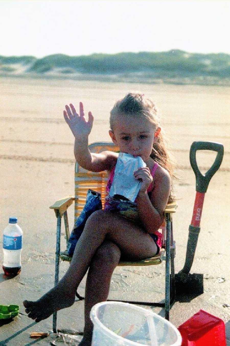 A little girl sits in a lawn chair sipping a juice pouch