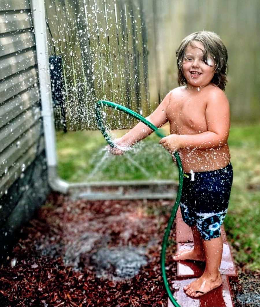 A little boy sprays hose water on himself
