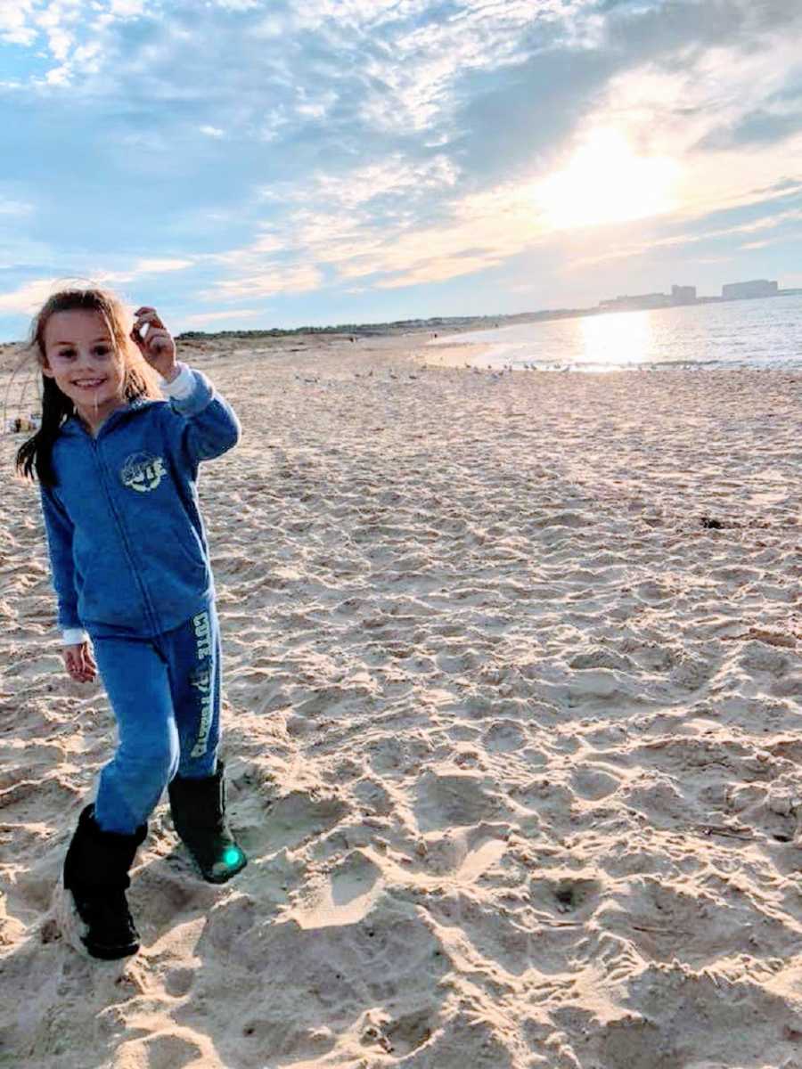 A little girl stands by herself on a beach wearing blue