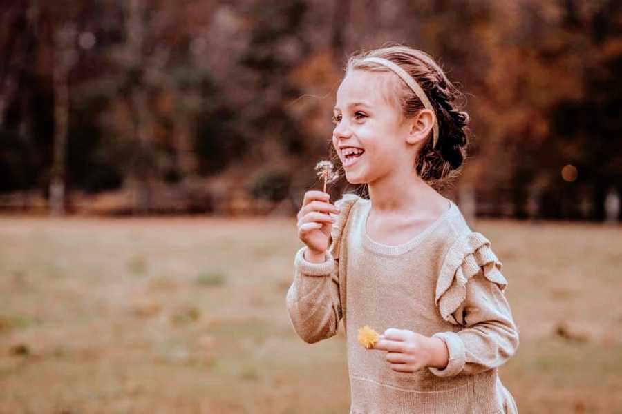 A little girl blows on a dandelion in a field