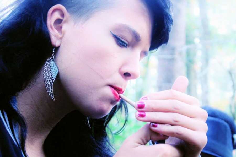 A person wearing earrings smokes a cigarette
